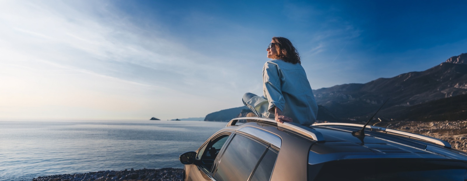 Woman sitting on the roof of her car at a coastal overlook at sunrise