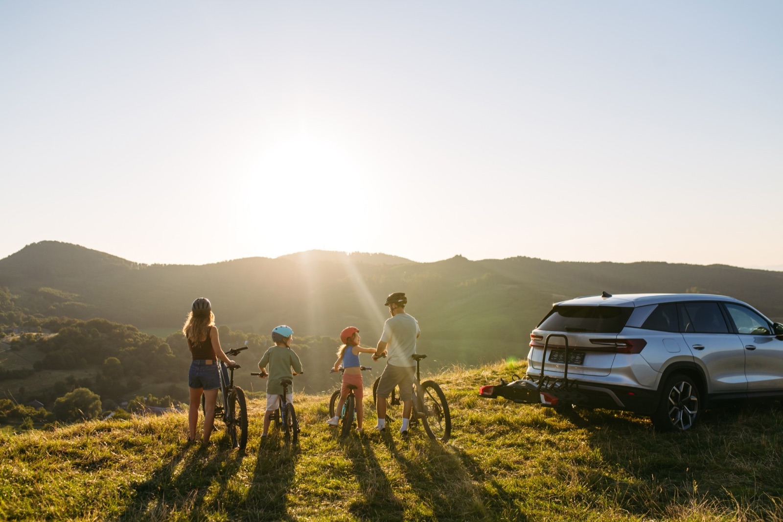 Family unloading bikes from their SUV on a hilltop at sunset