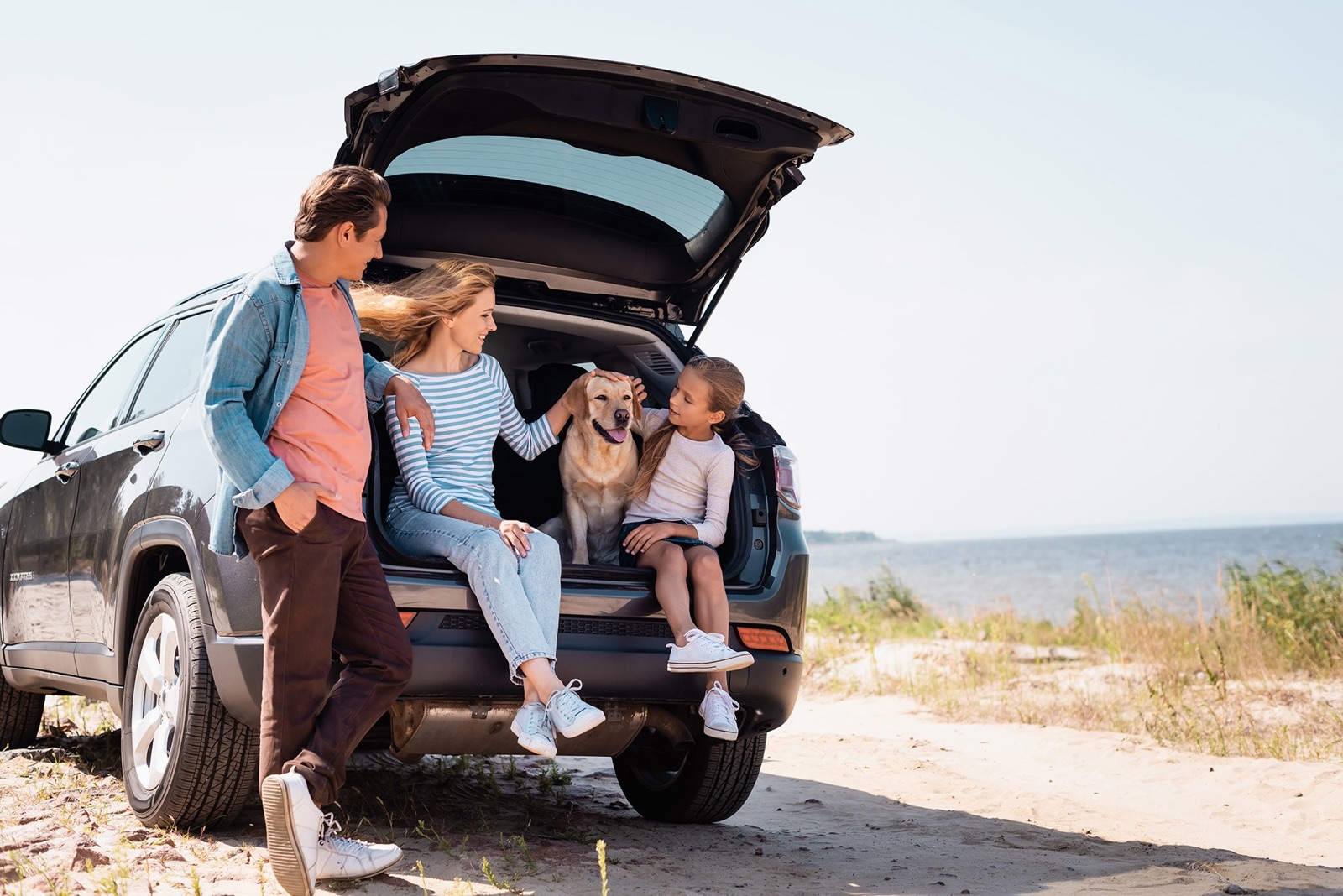 Family and their dog sitting in the open tailgate of an SUV by the shore — optional vehicle protection plans